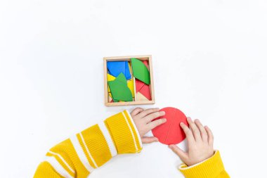 Kızların elinin en üst görüntüsü, Montessori okulundaki renkli ahşap geometrik şekiller bulmacasını çözmek ve oynamaktır. Matematiksel geometri kullanma kavramı çocuk eğitimi için kaynak öğrenme kavramı.