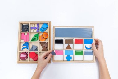 Kızların elinin en üst görüntüsü, Montessori okulundaki renkli ahşap geometrik şekiller bulmacasını çözmek ve oynamaktır. Öğrenme kaynaklarını çocuk eğitim dili ve yazımı için kullanma kavramı.