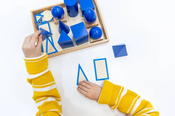 Kızların elinin en üst görüntüsü, Montessori okulundaki renkli ahşap geometrik şekiller bulmacasını çözmek ve oynamaktır. Matematiksel geometri kullanma kavramı çocuk eğitimi için kaynak öğrenme kavramı.