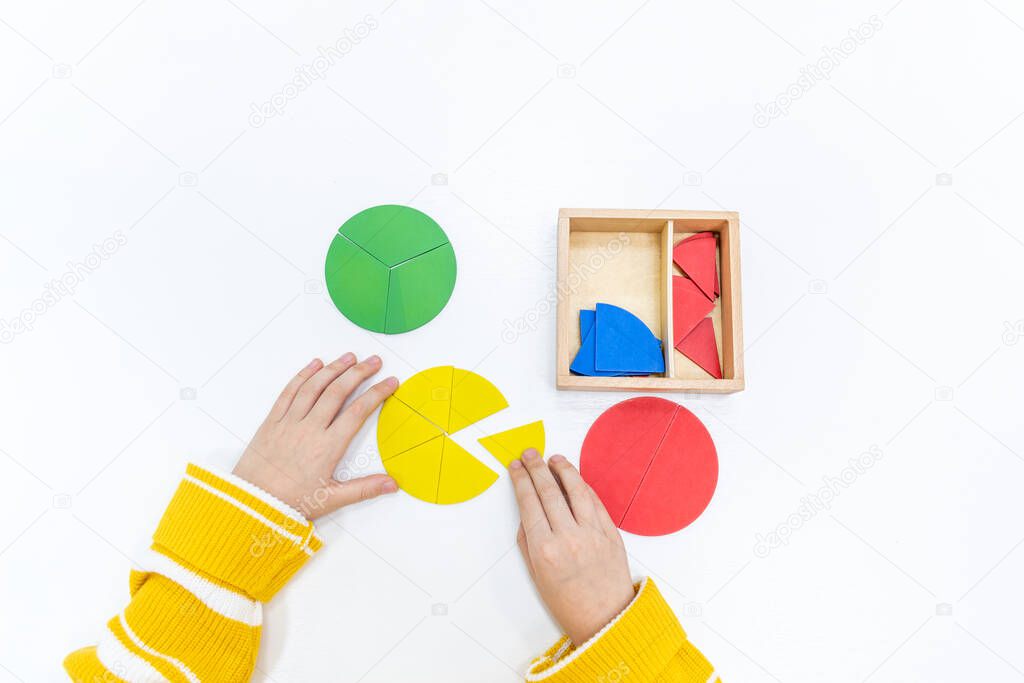 Top view of girls hand is playing and sorting a puzzle of colored wooden geometric shapes in montessori school. Concept of using a mathematical geometry learning resources for children education.
