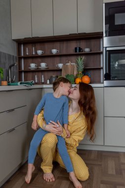 Genç anne küçük oğluna mutfakta sarılıyor. Evin içinde aile sağlığı var. Sabahları sağlıklı kahvaltı konsepti