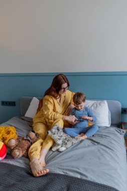 Genç anne ve oğlu çizgi film izliyorlar. Cep telefonu. Psikolojik sağlık konsepti. Sabah yatakta. Yaşam tarzını yavaşlatıyor