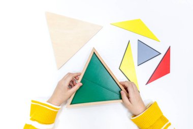 Kızların elinin en üst görüntüsü, Montessori okulundaki renkli ahşap geometrik şekiller bulmacasını çözmek ve oynamaktır. Matematiksel geometri kullanma kavramı çocuk eğitimi için kaynak öğrenme kavramı.