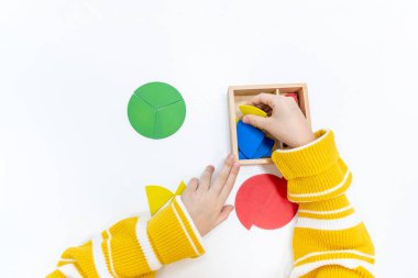 Kızların elinin en üst görüntüsü, Montessori okulundaki renkli ahşap geometrik şekiller bulmacasını çözmek ve oynamaktır. Matematiksel geometri kullanma kavramı çocuk eğitimi için kaynak öğrenme kavramı.