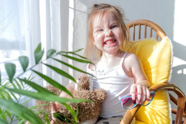 Defoktus. Küçük kız güneşin altında sallanan bir sandalyede oturur, kapalı alandaki bitkilerin arasında. Parlak gölge. Samimi insanlar konsepti. Evde dinlen.