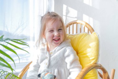 Defoktus. Küçük kız güneşin altında sallanan bir sandalyede oturur, kapalı alandaki bitkilerin arasında. Parlak gölge. Samimi insanlar konsepti. Evde dinlen.