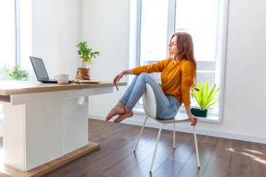 Genç iş kadını işten sonra internetten bilgisayar kullanarak meditasyon yapıyor. Dişi kız dizüstü bilgisayarın yanında sakin müzik dinler. Ev konforu ve ruh sağlığı konsepti.