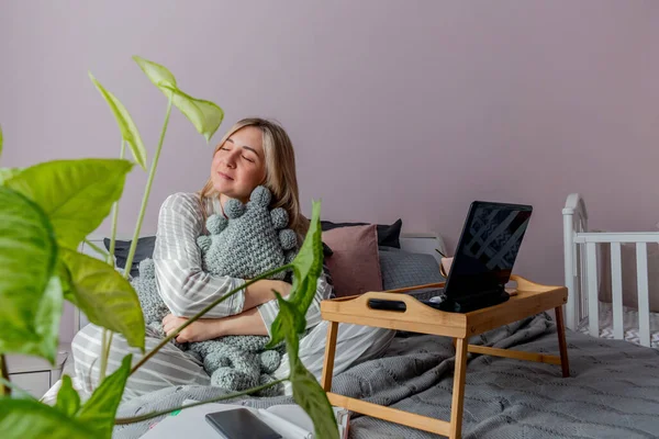 Genç iş kadını, işten sonra internette bilgisayar kullanarak yatakta otururken meditasyon yapıyor. Kız dizüstü bilgisayarın yanında sakin müzik dinliyor. Ev konfor bölgesi ve sağlık konsepti.