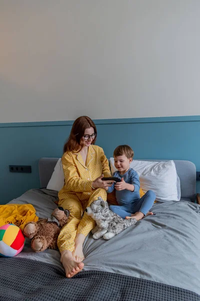 Genç anne ve oğlu arkadaşlarıyla video bağlantısı ile iletişim kuruyor. Cep telefonuyla konuşma. Psikolojik sağlık konsepti. Sabah yatakta.