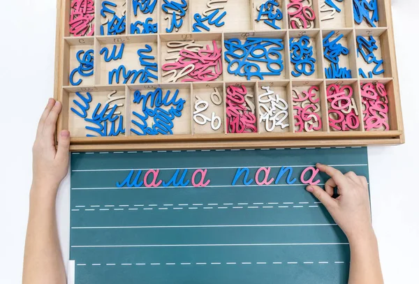 Çocukların, tahta tepsideki renkli Montessori hareketli alfabesini kullanarak kelimelerin oluşturulduğu en iyi manzara. Öğrenme, el-göz koordinasyonu ve motor beceriler geliştirme kavramı.