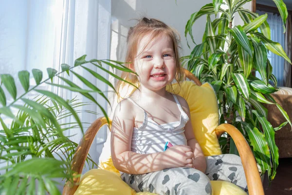 Defoktus. Küçük kız güneşin altında sallanan bir sandalyede oturur, kapalı alandaki bitkilerin arasında. Parlak gölge. Samimi insanlar konsepti. Evde dinlen.