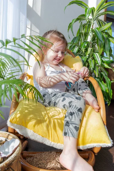 Defoktus. Küçük kız güneşin altında sallanan bir sandalyede oturur, kapalı alandaki bitkilerin arasında. Parlak gölge. Samimi insanlar konsepti. Evde dinlen.