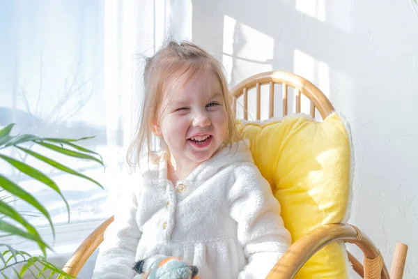 Defoktus. Küçük kız güneşin altında sallanan bir sandalyede oturur, kapalı alandaki bitkilerin arasında. Parlak gölge. Samimi insanlar konsepti. Evde dinlen.