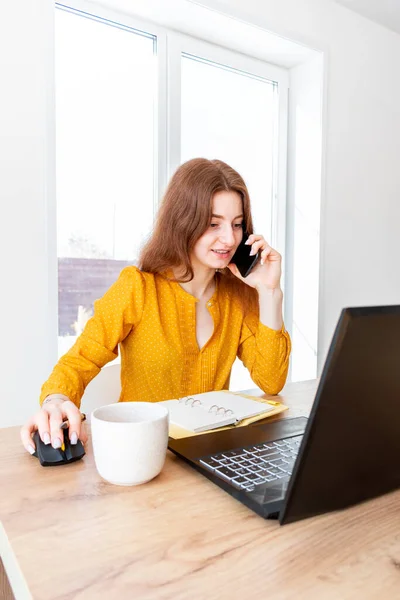 Defocus. Young business woman is using the computer and talking on the phone. Female girl looks into a laptop computer. Live broadcast concept. Comfort zone in the house.