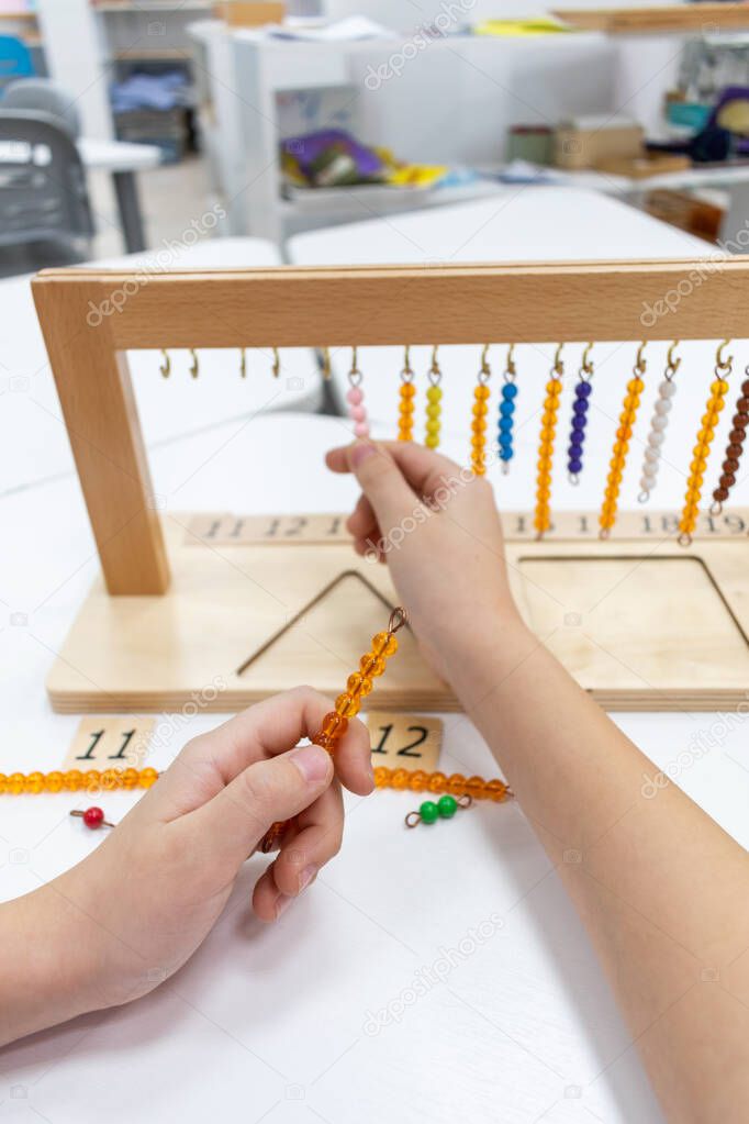 Girl in striped is playing and sorting a puzzle of colored plastic beads in montessori school. Concept of using a mathematical geometry learning resources children education.