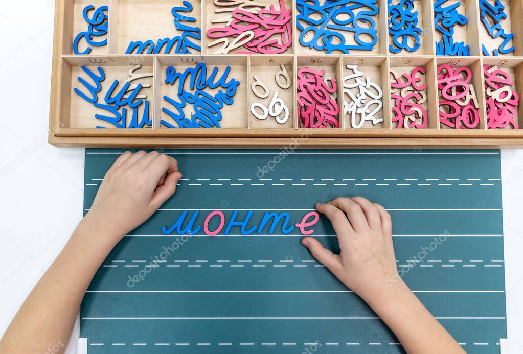 Top view of kids hands building words by using colored Montessori movable alphabet from the wooden tray on blackboard. Concept of learning,practicing hand-eye coordination and developing motor skills.