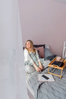 Genç iş kadını, işten sonra internette bilgisayar kullanarak yatakta otururken meditasyon yapıyor. Kız dizüstü bilgisayarın yanında sakin müzik dinliyor. Ev konfor bölgesi ve sağlık konsepti.