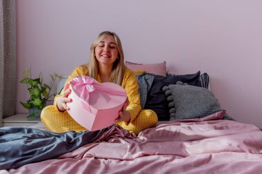 Genç kadın pijamalarıyla yatakta otururken hediyesini tutuyor. Ev refahı kavramı. Duygular yaşam tarzı