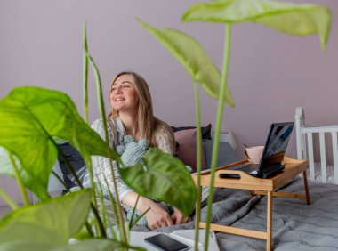 Genç iş kadını, işten sonra internette bilgisayar kullanarak yatakta otururken meditasyon yapıyor. Kız dizüstü bilgisayarın yanında sakin müzik dinliyor. Ev konfor bölgesi ve sağlık konsepti.