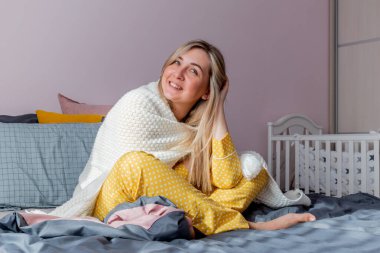 Genç kadın yatak odasında yatarken beyaz ekose kumaşa sarılmış. Sağlık ve akıl sağlığı konsepti. Sakin pastel renkler.