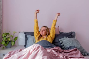 Genç bir kadın rahat bir yatakta otururken esniyor. Evim gibi. Refah kavramı.