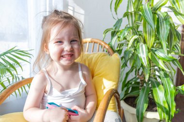 Defoktus. Küçük kız güneşin altında sallanan bir sandalyede oturur, kapalı alandaki bitkilerin arasında. Parlak gölge. Samimi insanlar konsepti. Evde dinlen.
