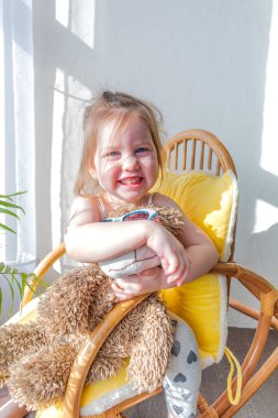 Defoktus. Küçük kız güneşin altında sallanan bir sandalyede oturur, kapalı alandaki bitkilerin arasında. Parlak gölge. Samimi insanlar konsepti. Evde dinlen.