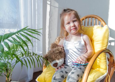 Defoktus. Küçük kız güneşin altında sallanan bir sandalyede oturur, kapalı alandaki bitkilerin arasında. Parlak gölge. Samimi insanlar konsepti. Evde dinlen.