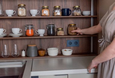 Uzay organizasyonu mutfak konsepti. İç kaplama, ekolojik bir tarz. Cam kavanozlu pürüzsüz raflar. Ağırlıklı tahıllar. Kadın eli makarna dolu kavanoza uzanıyor.