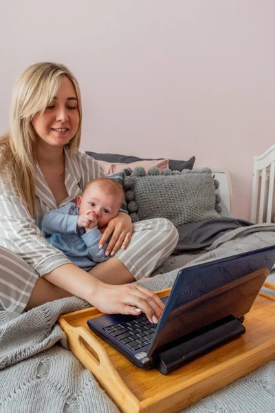 Mladá Žena Pohodlných Domácích Šatech Pracuje Notebooku Dítětem Náručí Ložnici — Stock fotografie