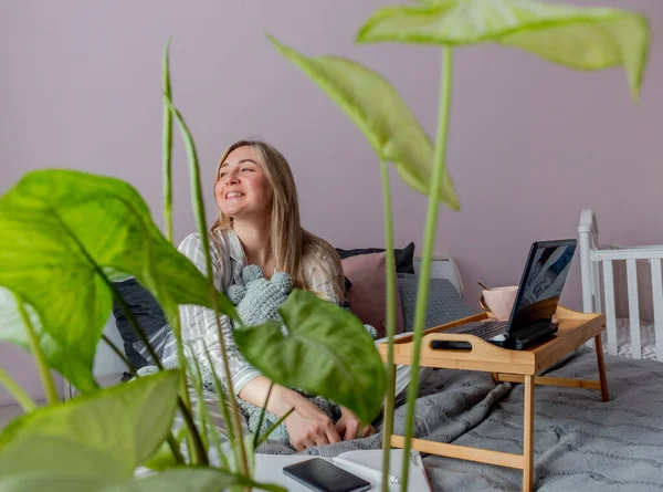Genç iş kadını, işten sonra internette bilgisayar kullanarak yatakta otururken meditasyon yapıyor. Kız dizüstü bilgisayarın yanında sakin müzik dinliyor. Ev konfor bölgesi ve sağlık konsepti.
