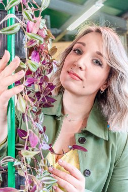 Sarı saçlı genç bir kadın serada duruyor ve bitkilere bakıyor. Doğal doğa. Sağlık konsepti Yeşil renk