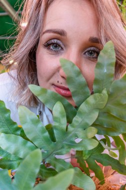 Sarı saçlı genç bir kadın serada duruyor ve bitkilere bakıyor. Doğal doğa. Sağlık konsepti Yeşil renk