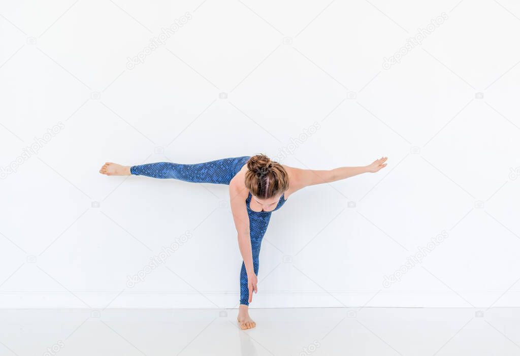 Young diverse woman practices yoga in a pose. Standing on the floor. White studio loft. Sport and wellbeing concept. Copy space