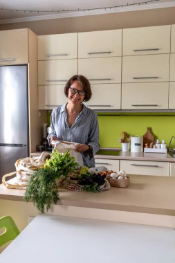 Yetişkin bir kadın, kumaş torbalarından çiftçi pazarından alınmış ürünleri çıkarıyor. Çevre dostu alışveriş. Sıfır atık. Bilinçli tüketim.