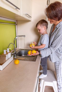 Yetişkin bir kadın ve oğlu mutfakta dururken sebze yıkıyorlar. Vejetaryen yemeği. Sıfır atık. Çiftlik sebzeleri
