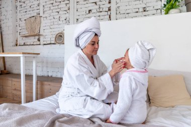 Beyaz cüppeli bir anne kızının yüzüne kozmetik maske sürüyor. Sağlık konsepti. Evde geçirilen zaman.