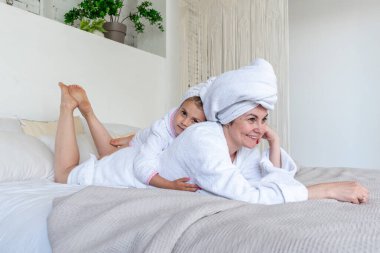 Anne ve kızı beyaz bornoz giyip yatakta otururken sarılıyorlar. Aile içinde hemşire iletişimi. Refah kavramı.