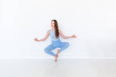 Yoga yapan çekici bir kadın. Nilüfer çiçeğinin üzerinde oturmak Utkatasana 'nın bir varyasyonudur. Spor giyim üzerine antrenman. Beyaz çatı katı stüdyo geçmişi