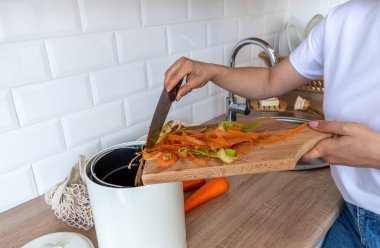 Yetişkin bir kadın sebze temizlemeyi gübre kovasına koyar. İnsanlar vejetaryen. Ev mutfağı. Sıfır atık. Bilinçli sebze tüketimi