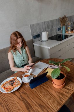 Defoktus. Genç bir kadın öğle yemeği sırasında bilgisayarla eğitimini internetten alıyor. Serbest çalışan bir kadın dizüstü bilgisayarda geziniyor. Aşırı bilgi yüklenmesi kavramı. Teknoloji ve insanlar. Evde Konfor Bölgesi.