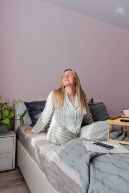 Genç iş kadını, işten sonra internette bilgisayar kullanarak yatakta otururken meditasyon yapıyor. Kız dizüstü bilgisayarın yanında sakin müzik dinliyor. Ev konfor bölgesi ve sağlık konsepti.