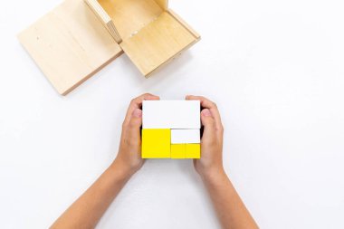 Kızların elinin en üst görüntüsü, Montessori okulundaki renkli ahşap geometrik şekiller bulmacasını çözmek ve oynamaktır. Matematiksel geometri kullanma kavramı çocuk eğitimi için kaynak öğrenme kavramı.