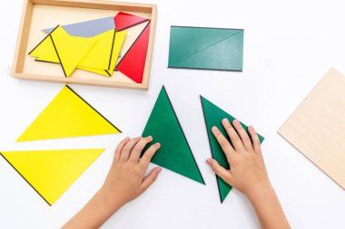 Kızların elinin en üst görüntüsü, Montessori okulundaki renkli ahşap geometrik şekiller bulmacasını çözmek ve oynamaktır. Matematiksel geometri kullanma kavramı çocuk eğitimi için kaynak öğrenme kavramı.
