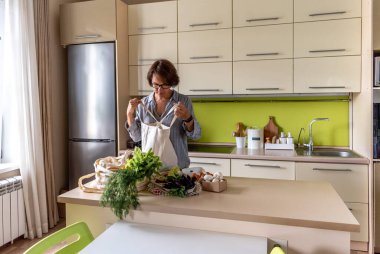 Yetişkin bir kadın, kumaş torbalarından çiftçi pazarından alınmış ürünleri çıkarıyor. Çevre dostu alışveriş. Sıfır atık. Bilinçli tüketim.