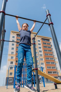 Genç kız oyun parkındaki bara tırmanıyor. Çocuk sporları konsepti. Sağlıklı bir yaşam tarzı. Boşluğu kopyala.