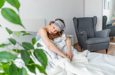 İpek pijamalı genç kadın rahat bir yatakta otururken esniyor. Evim gibi. Sağlık konsepti. Boşluğu kopyala