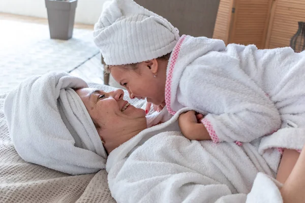 母と娘はベッドに座っている間に抱きつく白いテリーローブで服を着ています 家族内での看護コミュニケーション ウェルネスコンセプト — ストック写真