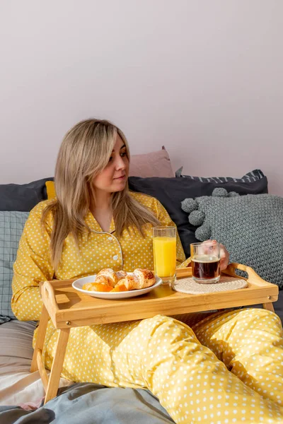 黄色のパジャマの若い女性は ベッドルームでベッドに横になっている間 健康的な朝食を持っています 家庭の幸福の概念 若い女性の感情的な健康 — ストック写真