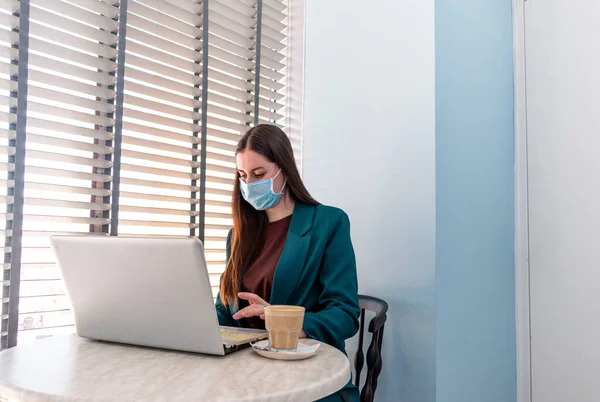 Young woman in suite with protective mask is working on computer. Businesswoman is keeping social distancing and working remotely. New normal concept